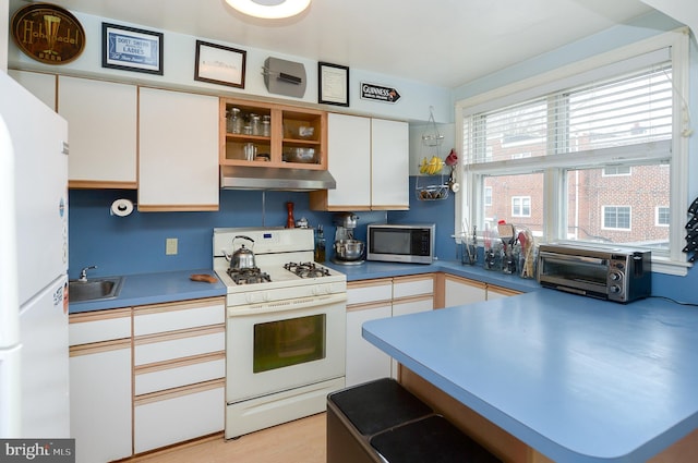 kitchen with white cabinetry, white appliances, kitchen peninsula, and sink