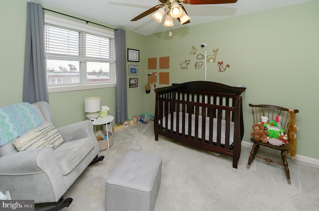 carpeted bedroom featuring a crib and ceiling fan