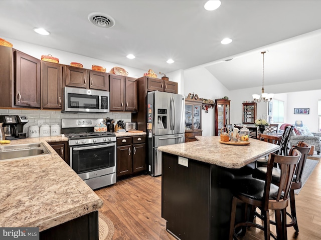 kitchen featuring appliances with stainless steel finishes, sink, a kitchen bar, hanging light fixtures, and light wood-type flooring