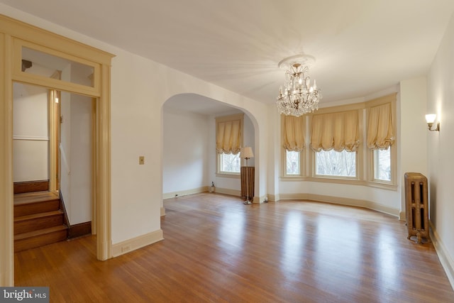 empty room featuring radiator, hardwood / wood-style floors, and a chandelier