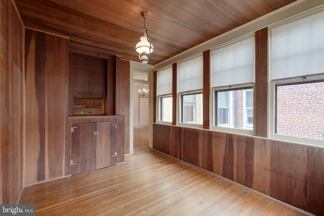 empty room featuring an inviting chandelier, light hardwood / wood-style flooring, wooden ceiling, and wood walls