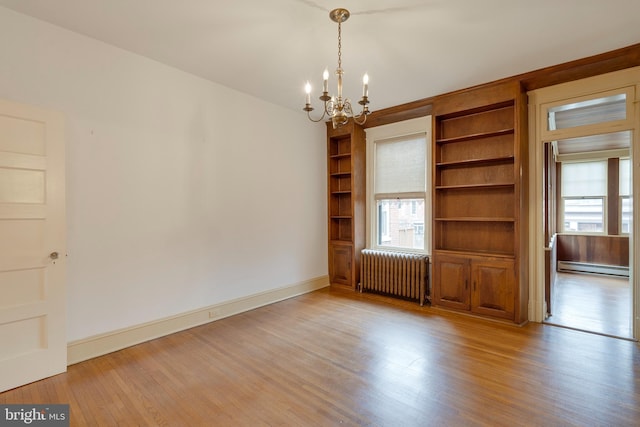 empty room featuring radiator, a notable chandelier, a baseboard radiator, and light wood-type flooring