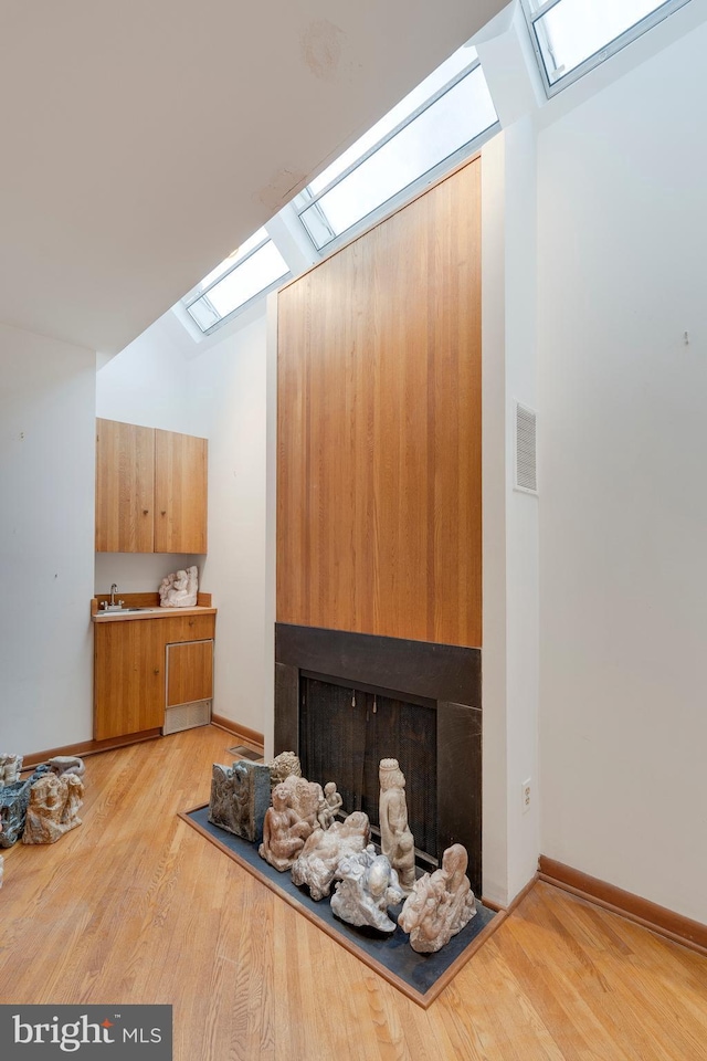 living room with sink, lofted ceiling with skylight, and light hardwood / wood-style floors