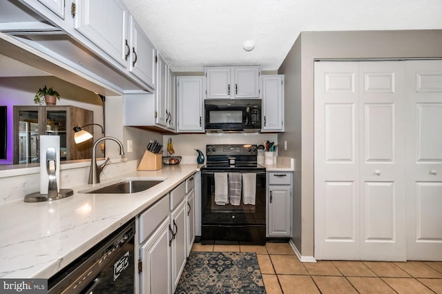 kitchen with sink, light tile patterned floors, black appliances, light stone countertops, and a textured ceiling