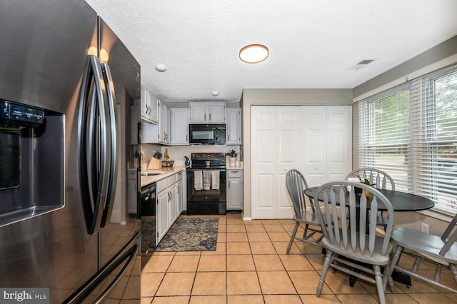 kitchen featuring gray cabinets, light tile patterned floors, a textured ceiling, and black appliances