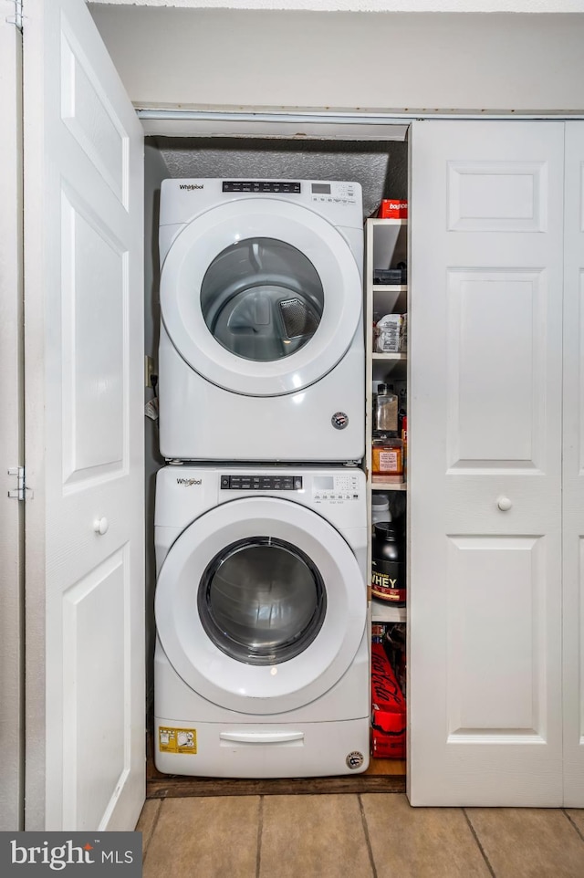 laundry area with stacked washer / drying machine and light tile patterned floors