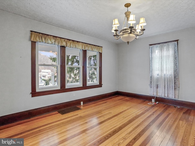 empty room featuring a chandelier, hardwood / wood-style floors, and a textured ceiling