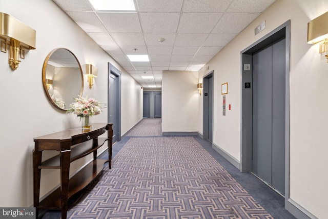 corridor with dark colored carpet, a paneled ceiling, and elevator