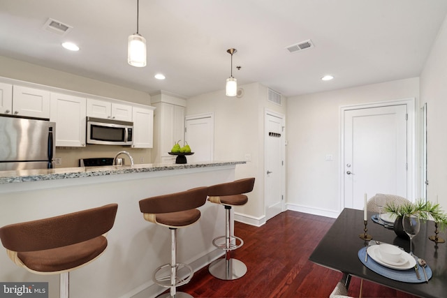 kitchen featuring white cabinetry, appliances with stainless steel finishes, pendant lighting, and light stone counters