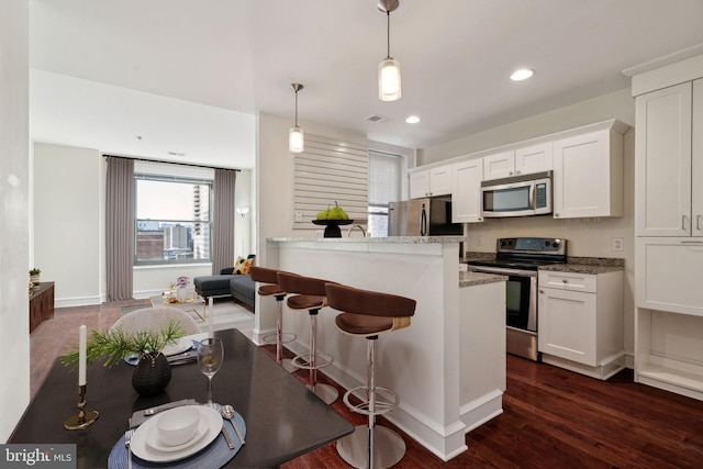 kitchen featuring pendant lighting, light stone counters, white cabinetry, and appliances with stainless steel finishes