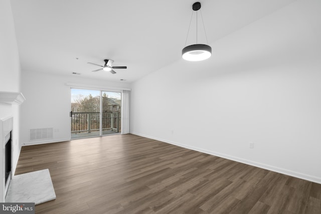 unfurnished living room with a premium fireplace, dark wood-type flooring, and ceiling fan