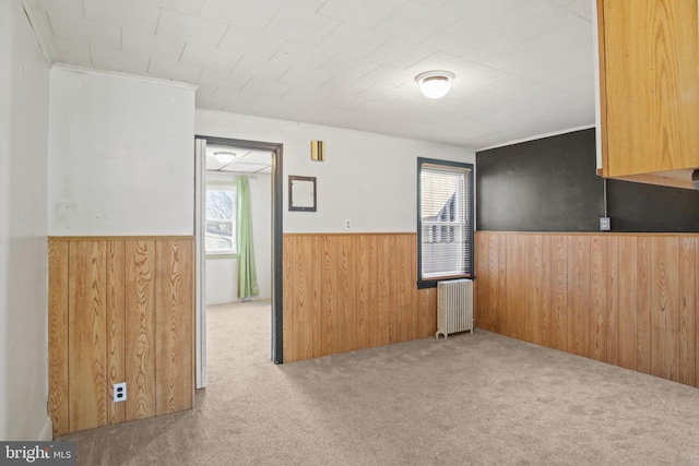 empty room featuring crown molding, light colored carpet, radiator, and wood walls