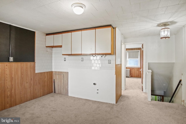 kitchen featuring light carpet, hanging light fixtures, wooden walls, radiator, and white cabinets