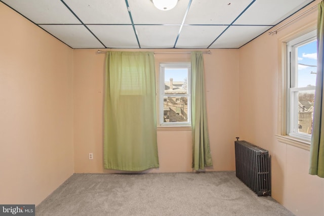 carpeted empty room with a paneled ceiling and radiator