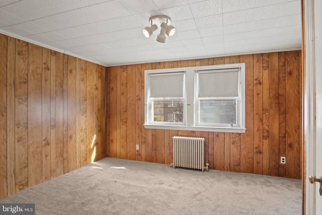 spare room featuring carpet floors, radiator heating unit, and wood walls