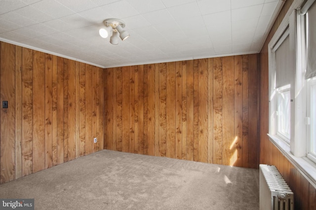 carpeted empty room featuring radiator heating unit and wooden walls