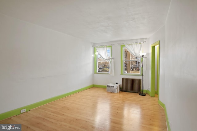 unfurnished room with a wall mounted AC, radiator heating unit, and light wood-type flooring