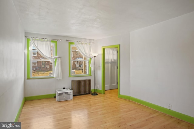 unfurnished room with radiator heating unit, light hardwood / wood-style floors, and a wall mounted AC