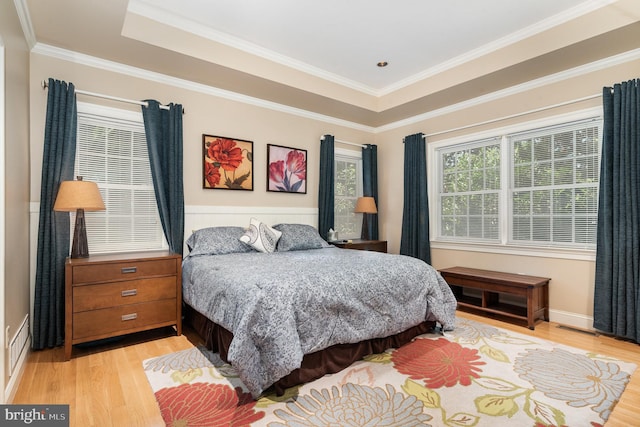 bedroom featuring ornamental molding, a raised ceiling, and light wood-type flooring