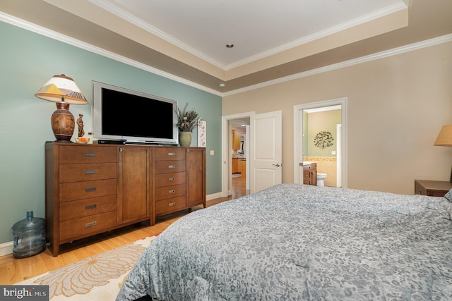 bedroom with crown molding, ensuite bath, a tray ceiling, and light hardwood / wood-style floors