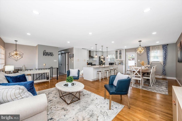 living room with recessed lighting, light wood-style flooring, baseboards, and a barn door