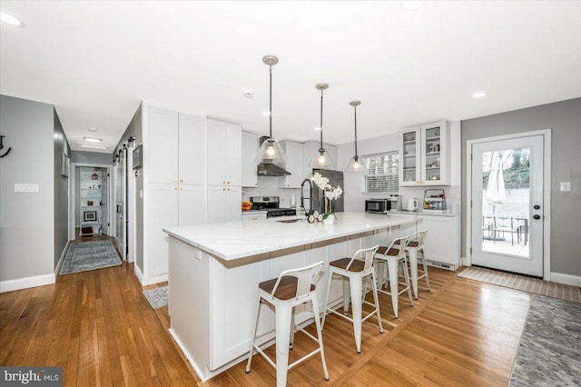 kitchen with a barn door, glass insert cabinets, hanging light fixtures, a kitchen island with sink, and white cabinetry