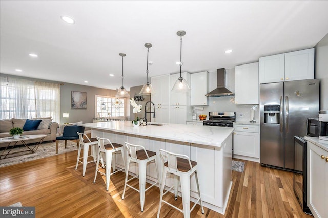 kitchen with an island with sink, wall chimney range hood, appliances with stainless steel finishes, and white cabinets