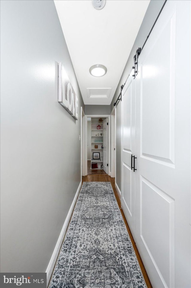 corridor with wood finished floors, baseboards, and a barn door