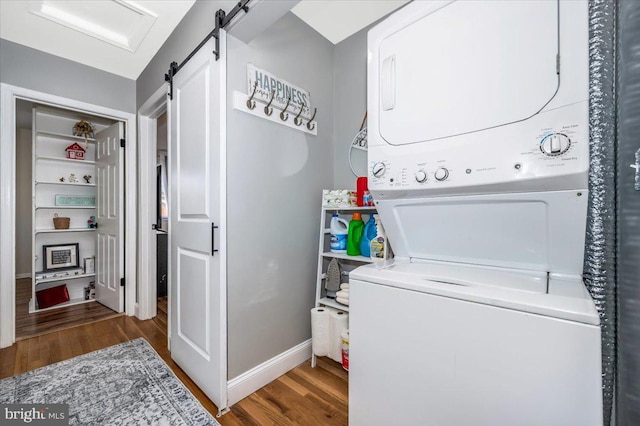 clothes washing area featuring a barn door, laundry area, wood finished floors, baseboards, and stacked washer / drying machine