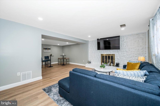 living room featuring a large fireplace, visible vents, baseboards, and wood finished floors