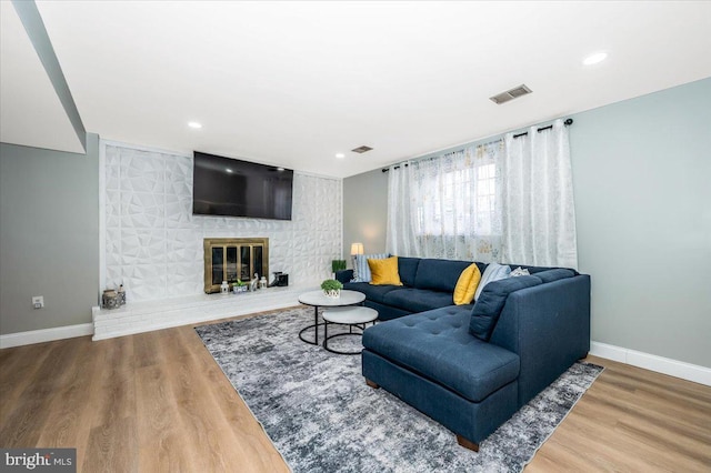 living room featuring a large fireplace, baseboards, visible vents, wood finished floors, and recessed lighting