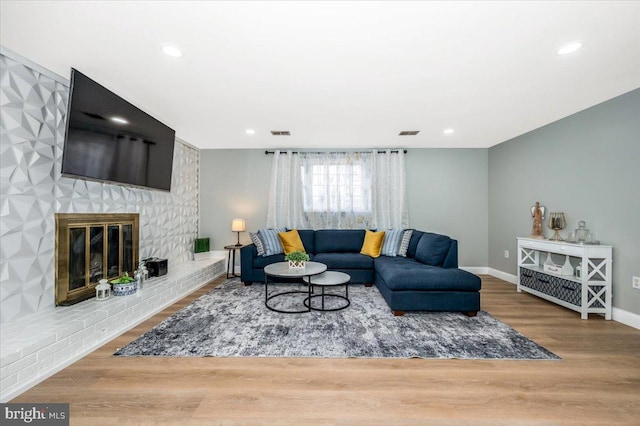 living room featuring a brick fireplace, baseboards, visible vents, and wood finished floors