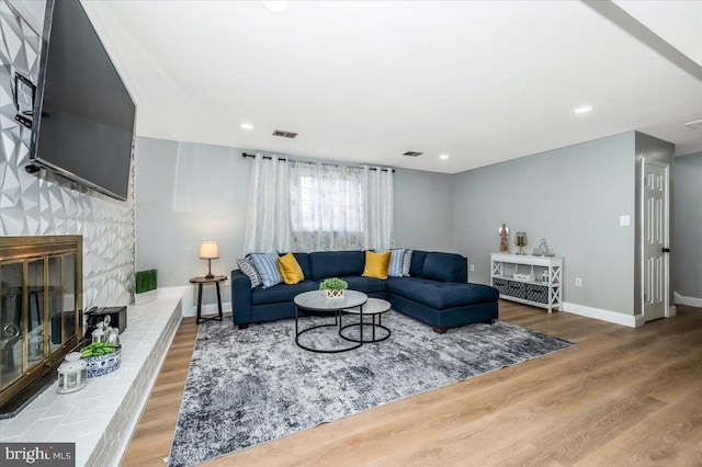 living area with visible vents, a stone fireplace, baseboards, and wood finished floors