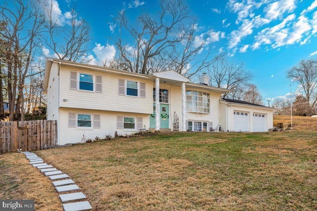 bi-level home featuring an attached garage, brick siding, fence, a chimney, and a front yard