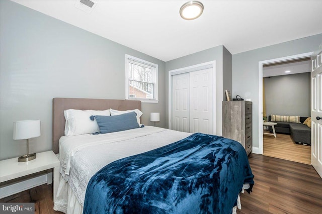 bedroom with a closet, visible vents, dark wood finished floors, and baseboards