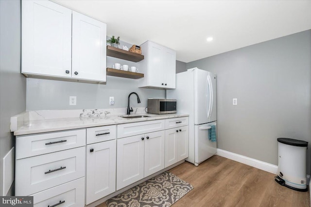 kitchen featuring baseboards, stainless steel microwave, white cabinetry, open shelves, and a sink