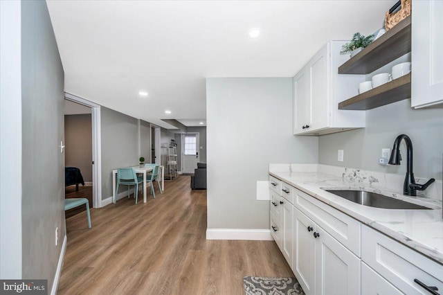 kitchen with white cabinets, light stone counters, open shelves, and a sink