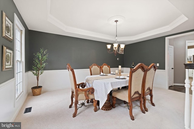 carpeted dining room featuring an inviting chandelier, crown molding, and a raised ceiling