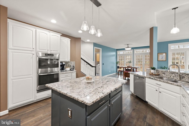 kitchen featuring decorative light fixtures, a center island, appliances with stainless steel finishes, light stone countertops, and white cabinets