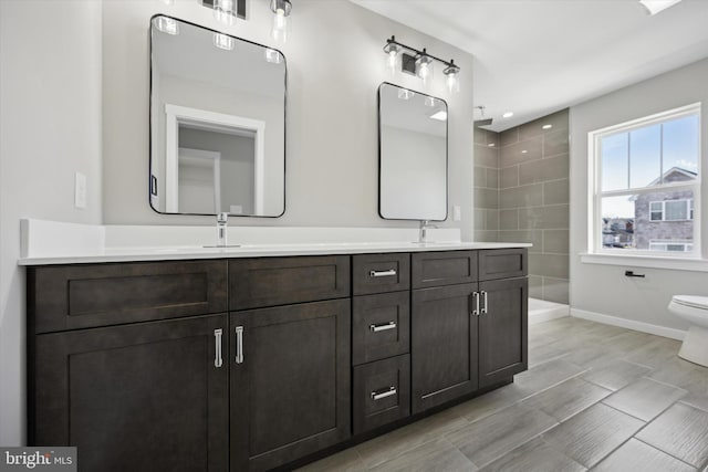 bathroom featuring baseboards, a sink, toilet, and double vanity