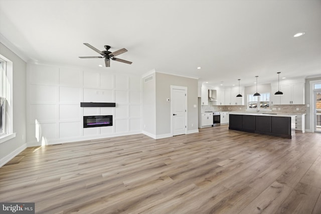 unfurnished living room featuring recessed lighting, ornamental molding, a glass covered fireplace, ceiling fan, and light wood-type flooring