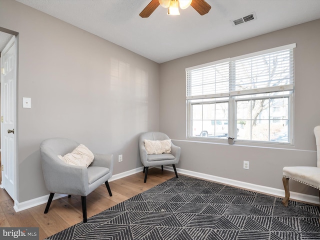 living area with ceiling fan, visible vents, baseboards, and wood finished floors