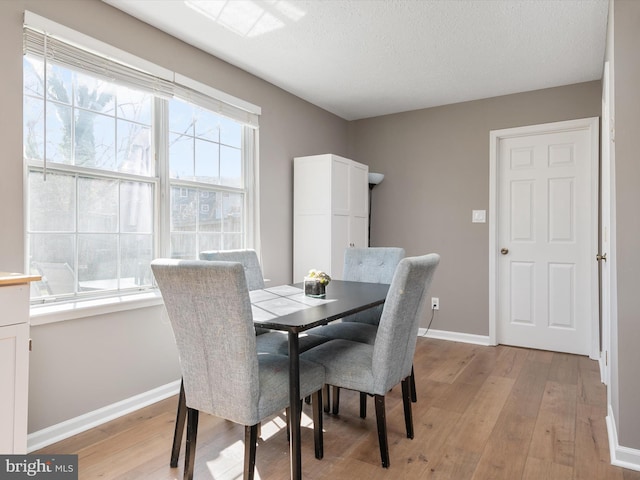 dining room featuring light wood finished floors, baseboards, and a textured ceiling