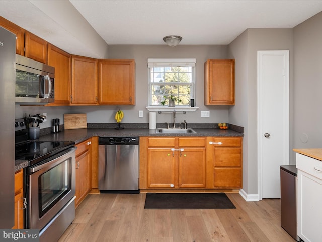 kitchen with light wood-type flooring, dark countertops, stainless steel appliances, and a sink