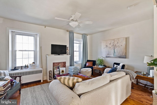 living room featuring ceiling fan, radiator, hardwood / wood-style floors, and a brick fireplace