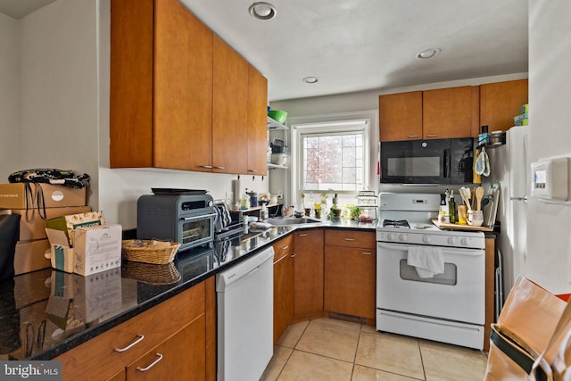 kitchen with light tile patterned flooring, sink, dark stone countertops, and white appliances