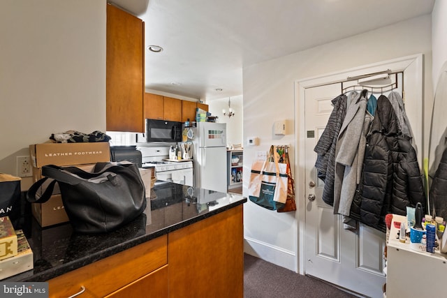 kitchen featuring dark carpet, dark stone countertops, a notable chandelier, and white appliances