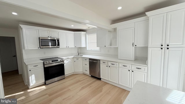 kitchen featuring sink, light hardwood / wood-style flooring, appliances with stainless steel finishes, white cabinetry, and light stone counters