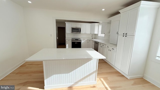 kitchen with stainless steel appliances, a center island, white cabinets, and light wood-type flooring