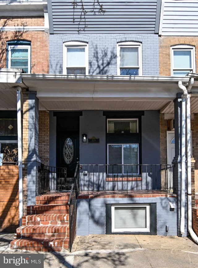 doorway to property with covered porch, brick siding, and an attached garage